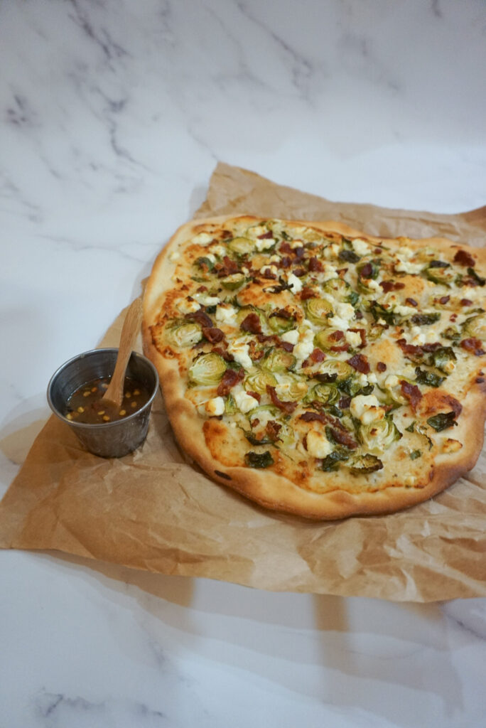 Prepared Bacon Brussel Sprout Goat Cheese Pizza with a spicy honey drizzle on the side.