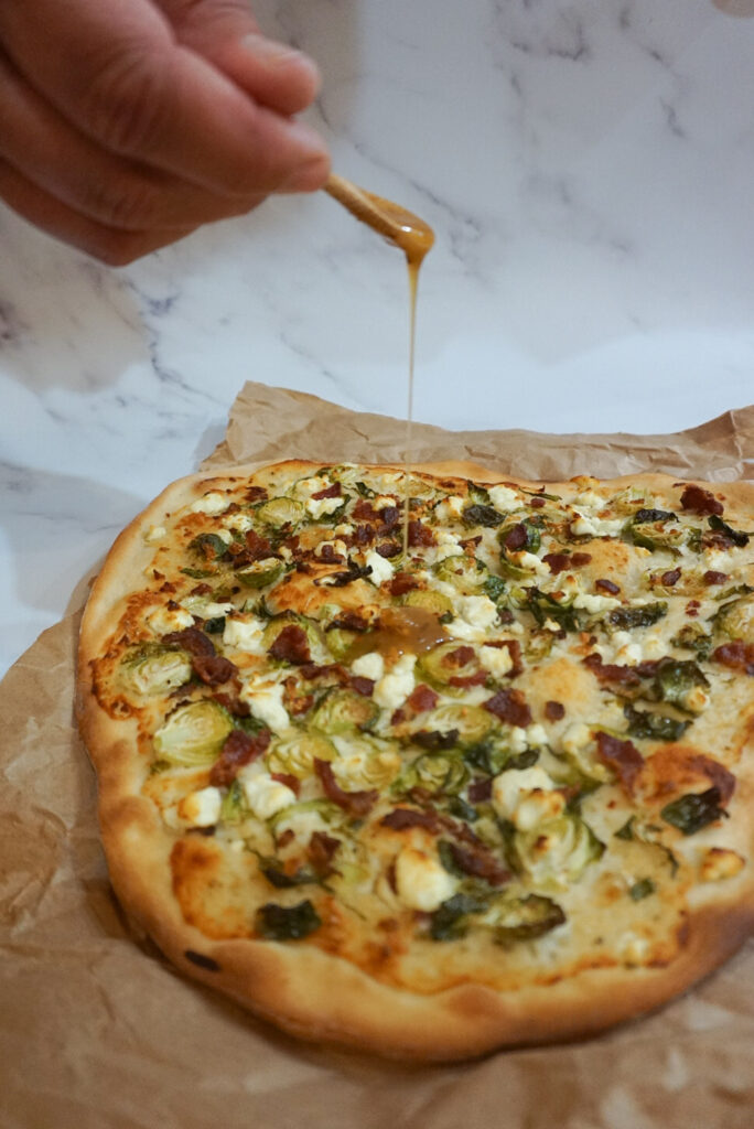 Drizzling spicy hot honey onto the Bacon Brussel Sprout Goat Cheese Pizza