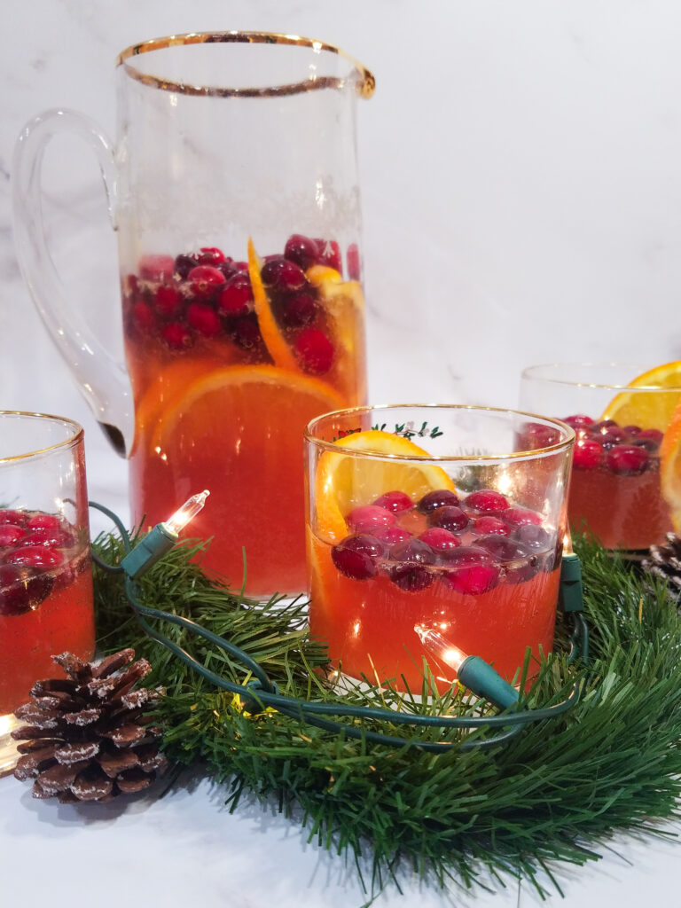 A straight on shot of a glass and pitcher full of Sparkling Cranberry Orange Sangria.