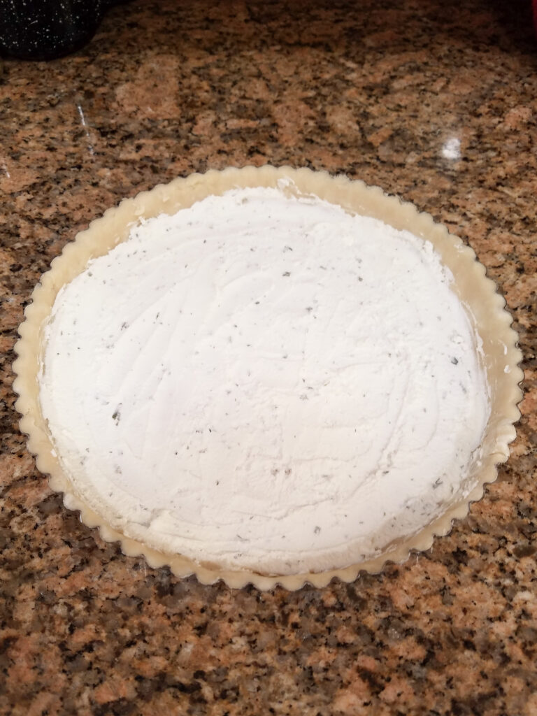 Goat cheese smeared on the bottom of the crust lined pie tin.