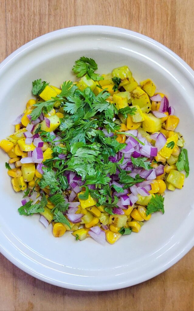 All of the prepared corn and squash salsa ingredients added to a bowl.