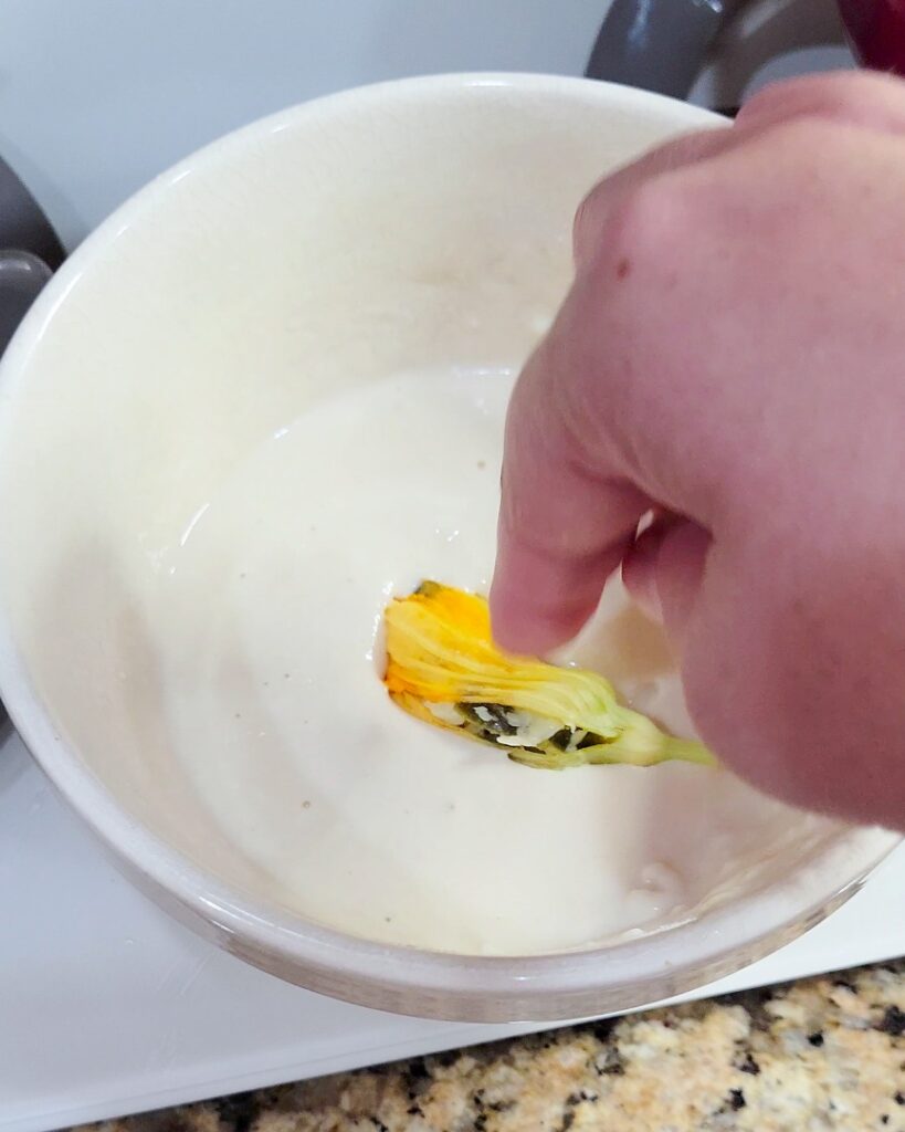 Dipping a stuffed blossom into beer batter. 