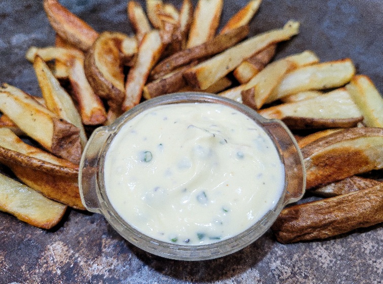 A cup of the best homemade ranch with baked french fries around it.